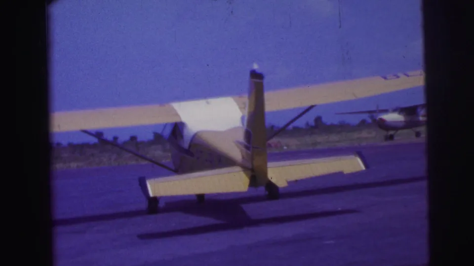 1967 Brazil 8mm frame with the small yellow and white aircraft seen from behind as it moves away on the runway.