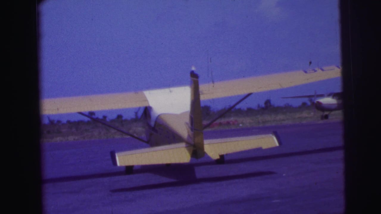 Small yellow and white plane seen from behind on a runway.