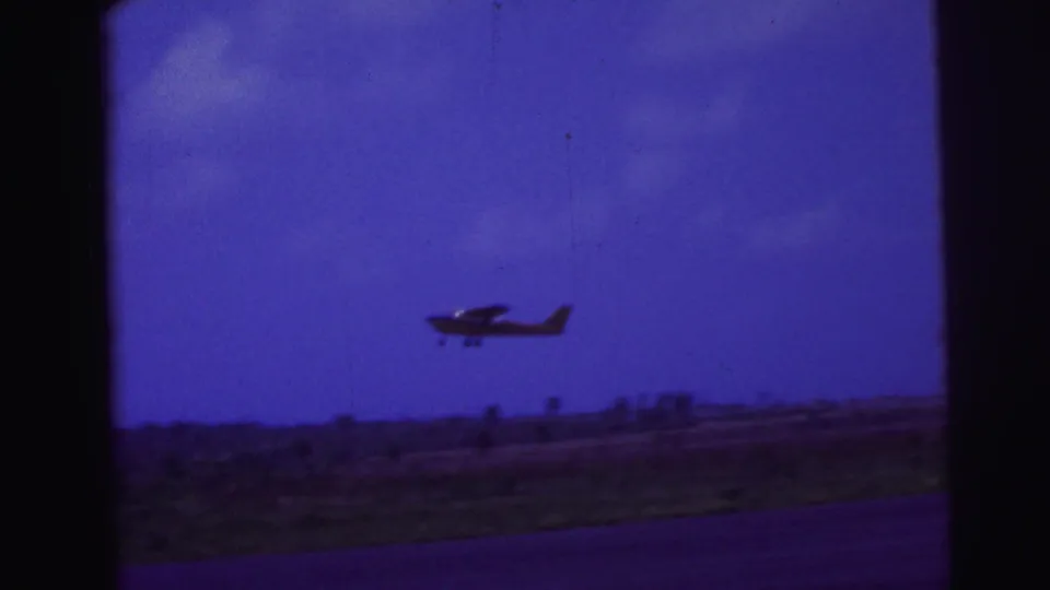 Small single-engine plane appears airborne over a low Brazil airfield horizon in a 1967 8mm frame.