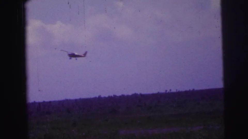 1967 Brazil home-movie frame with a small plane silhouetted against pale sky above a rural landscape.