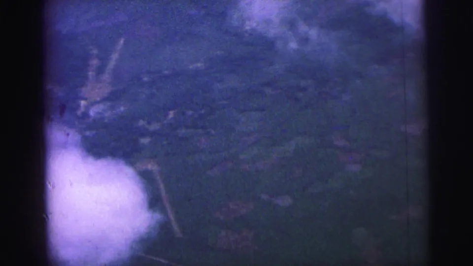 1967 Brazil 8mm frame with an overhead view of rural terrain, soft clouds, and dark gate or frame-edge shadow at center.