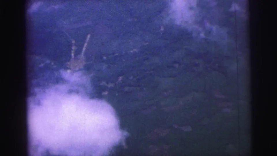 1967 Brazil 8mm frame showing a cloud bank over blue-green land, with small pale marks that may be roads or structures.