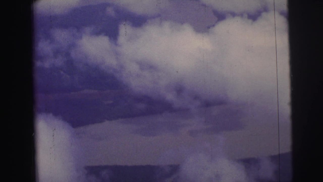 1967 Brazil home-movie aerial view with clouds partly covering land and water below, seen within dark film gate edges.