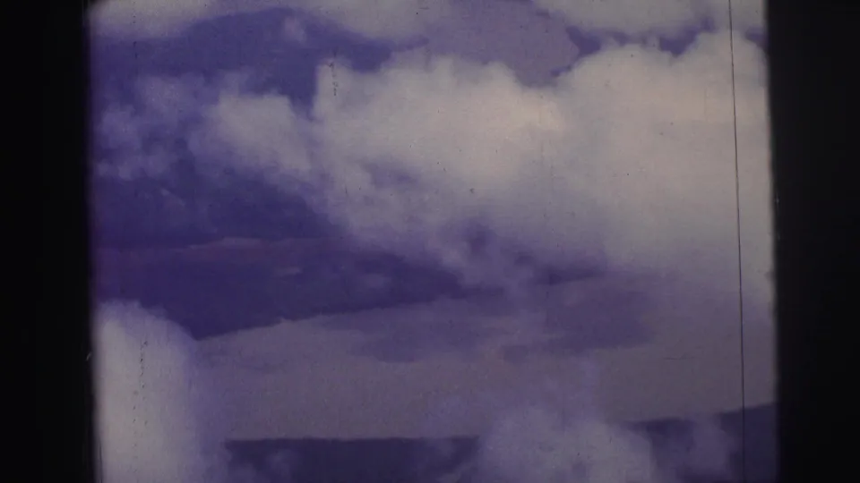 1967 Brazil home-movie aerial view with clouds partly covering land and water below, seen within dark film gate edges.