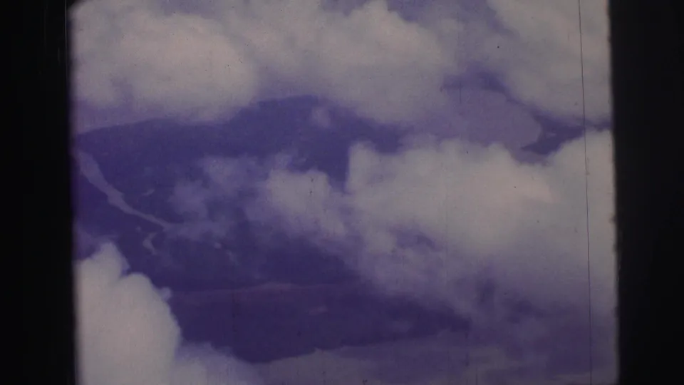 1967 Brazil airplane-window view with clouds, hazy land, and a winding river form visible through breaks in the cover.