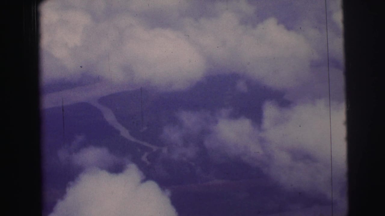 Clouds partly obscure a winding river and terrain seen through an airplane window.