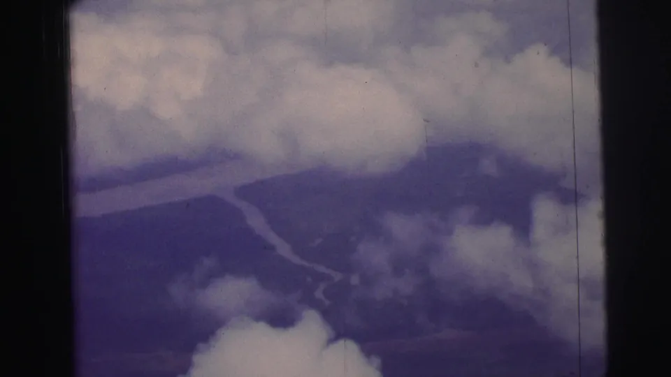 Aerial passenger-window view over Brazil, showing broken cloud cover and a river bend on 8mm film.