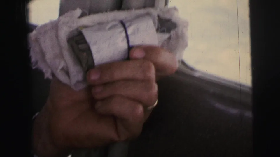 Inside an airplane over Brazil in 1967, a passenger hand holds a cloth-wrapped object near the window.