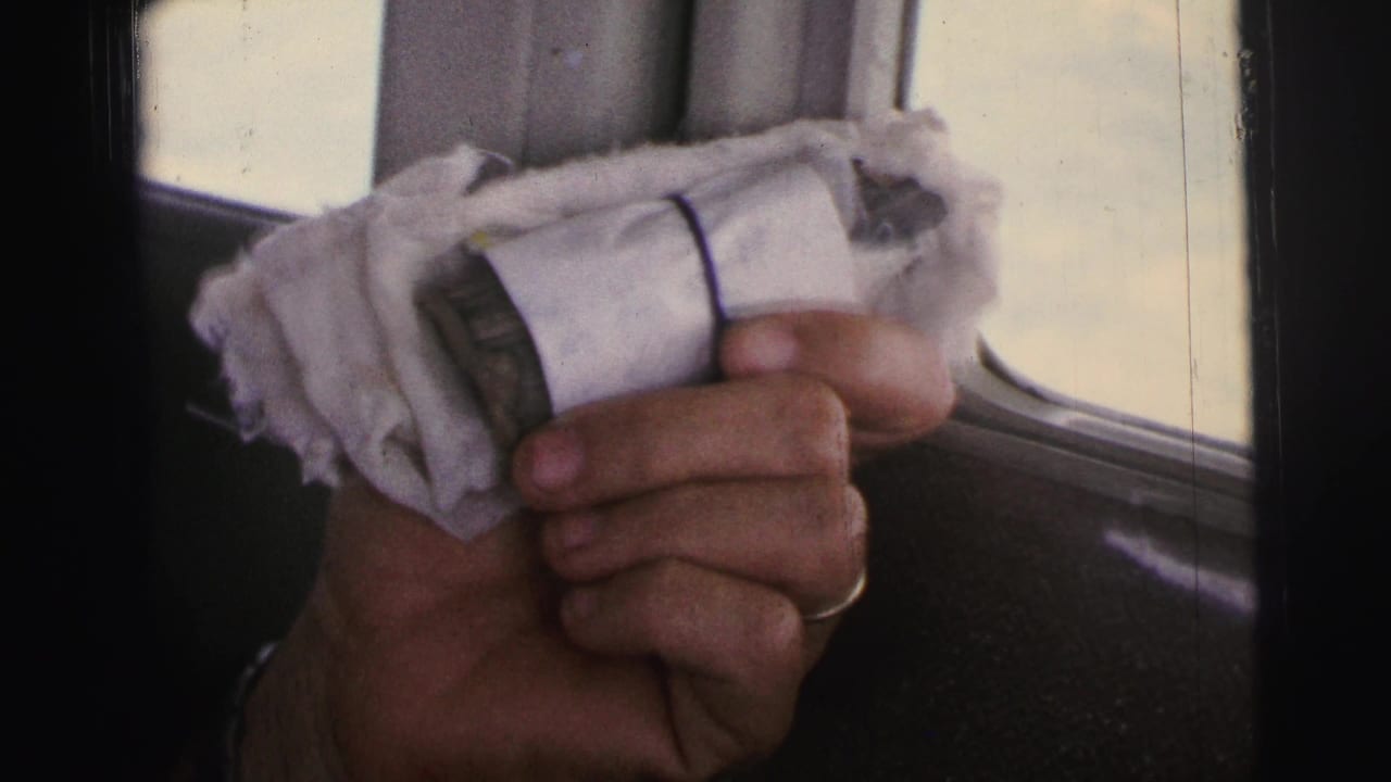 Hand with a ring holding a white cloth-wrapped bundle near an aircraft window.
