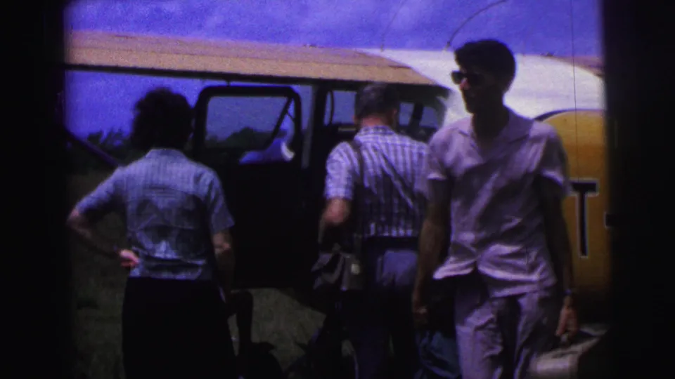 A woman and a man stand beside the open door of a small aircraft on a grassy Brazil airfield in 1967 footage.