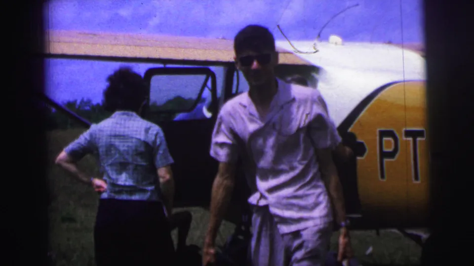 A man in sunglasses walks past a small aircraft with partial PT markings while another passenger stands near the open door.