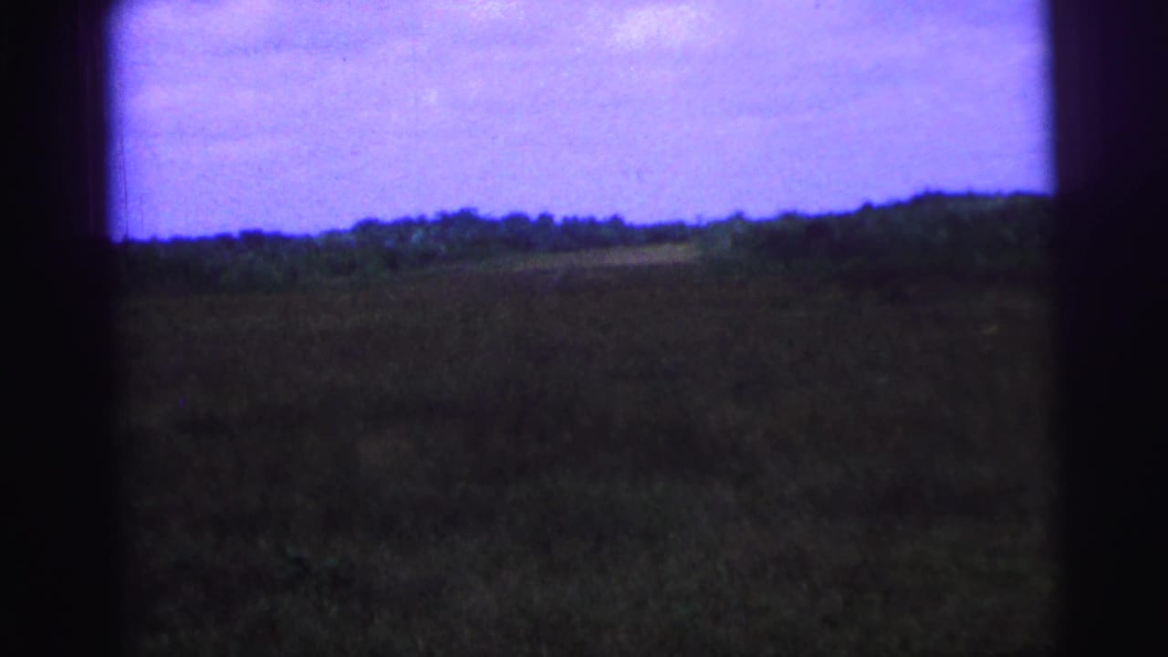 1967 Brazil 8mm frame with a distant tree line, open field, purple sky, and heavy dark frame edges.
