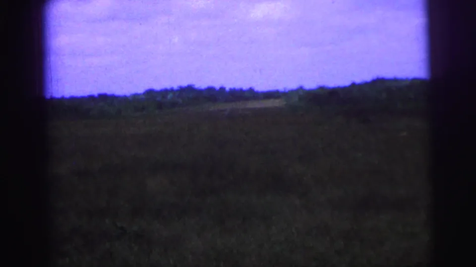 1967 Brazil 8mm frame with a distant tree line, open field, purple sky, and heavy dark frame edges.
