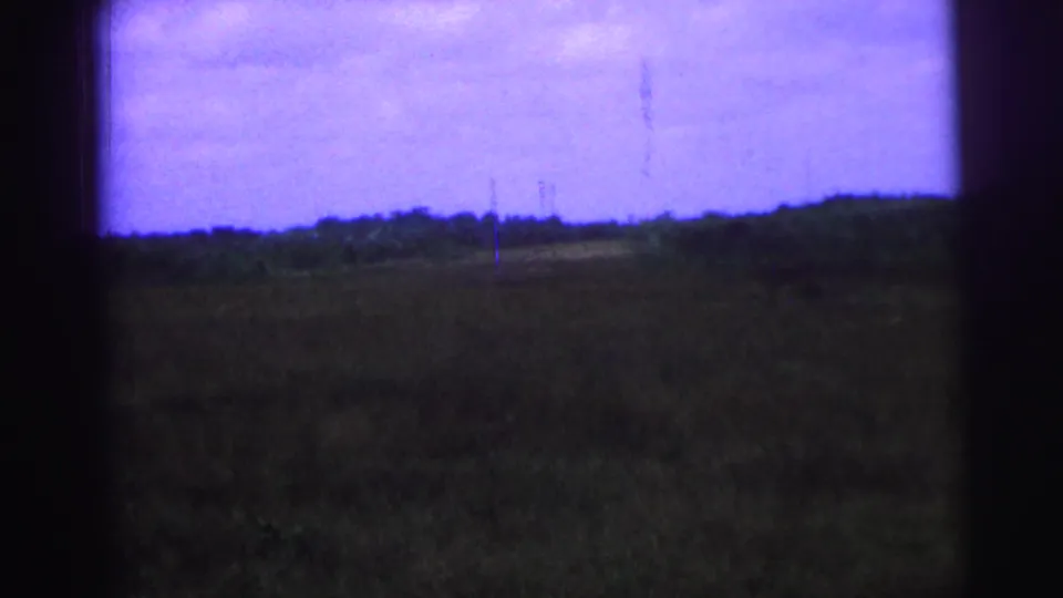 1967 Brazil 8mm view across a rural field toward a low tree line, with color shift and dark gate shadows.