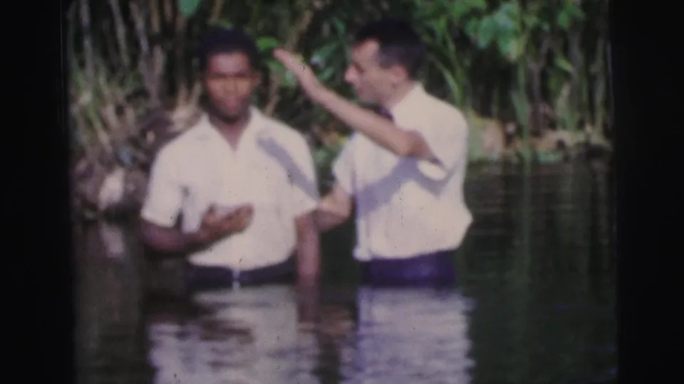 In the river, one man raises a hand beside another during an apparent baptismal ritual in Brazil.
