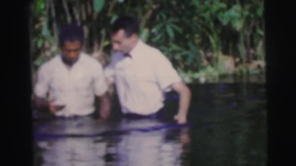 1967 Brazil 8mm frame showing two men waist-deep in water after an apparent baptism action.