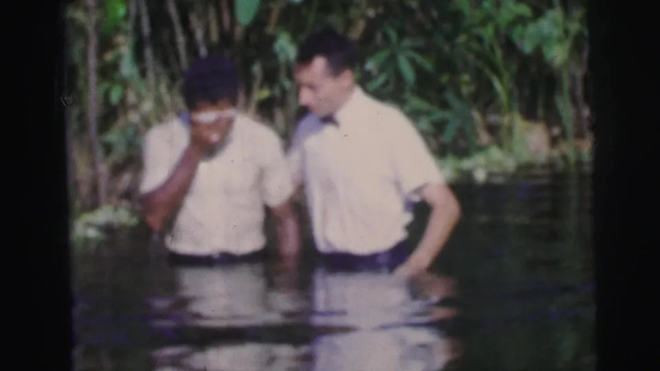 1967 Brazil 8mm frame of two men in water, one with a hand near his face, after an apparent baptism.
