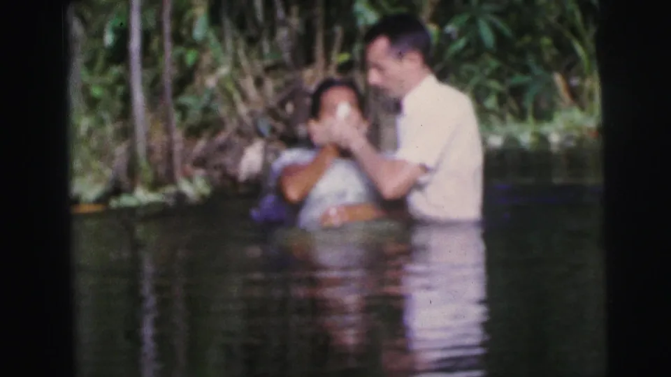 In the 1967 Brazil footage, the man appears to guide or support the woman as she leans back in the water during the ritual.