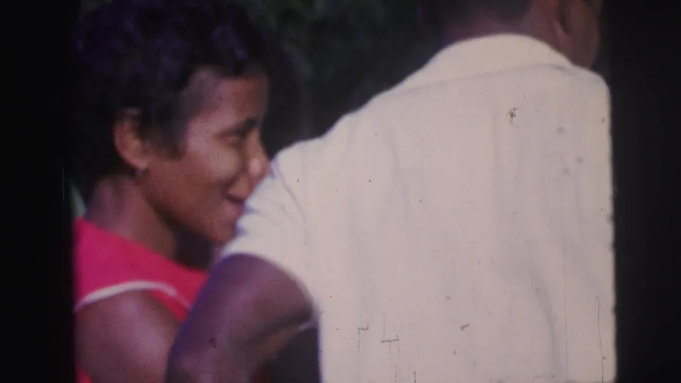 A close home-movie frame shows a woman in a red dress smiling near a person in a white shirt during the same outdoor ceremony.
