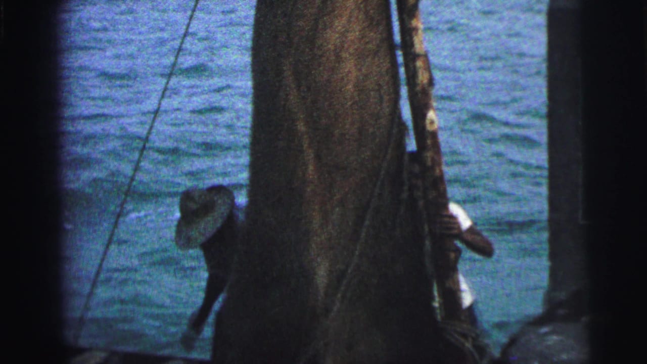 1967 Brazil 8mm frame showing men working around a sail and rigging on open water, partly obscured by dark film edges.