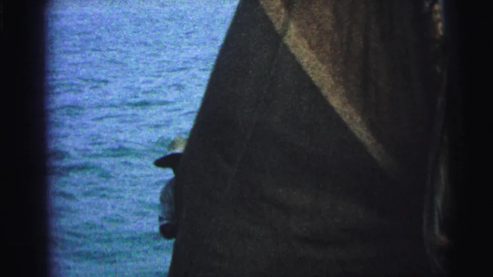1967 Brazil 8mm frame where the dark sail nearly covers the view, leaving a hat-wearing man and blue water partly visible.