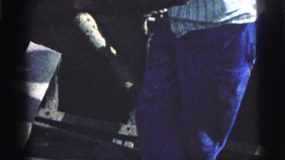 Close 8mm home-movie view of a sailor's lower body, rope, and shadowed deck surfaces during boat preparation in Brazil.