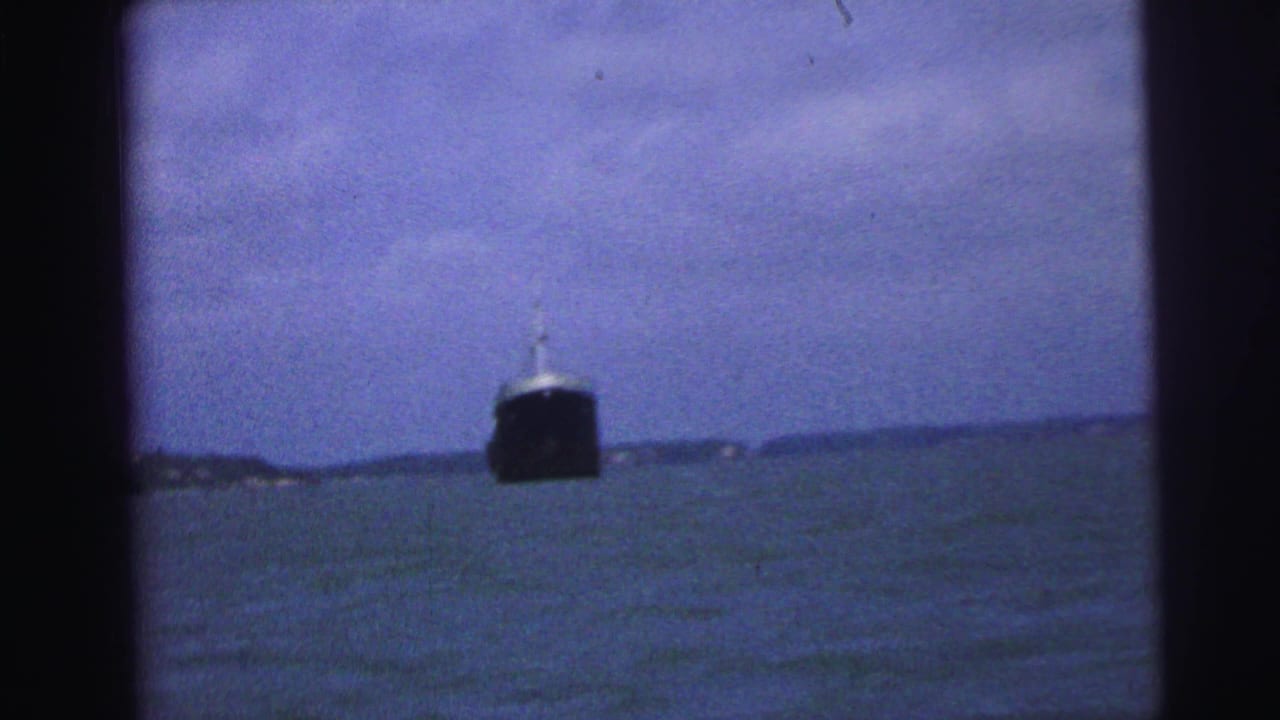 1967 Brazil 8mm frame showing a distant dark ship on rough water, viewed through dark foreground framing.