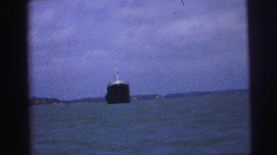 1967 Brazil 8mm frame showing a distant dark ship on rough water, viewed through dark foreground framing.