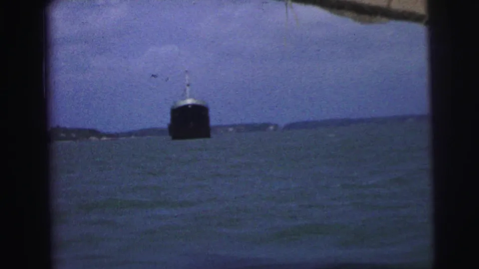 1967 Brazil home-movie view of a large vessel on choppy water, with a low shoreline and dark frame edges.