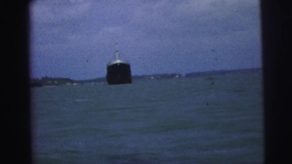 1967 Brazil 8mm frame of a dark ship beyond rough water, filmed from a moving or enclosed boat position.