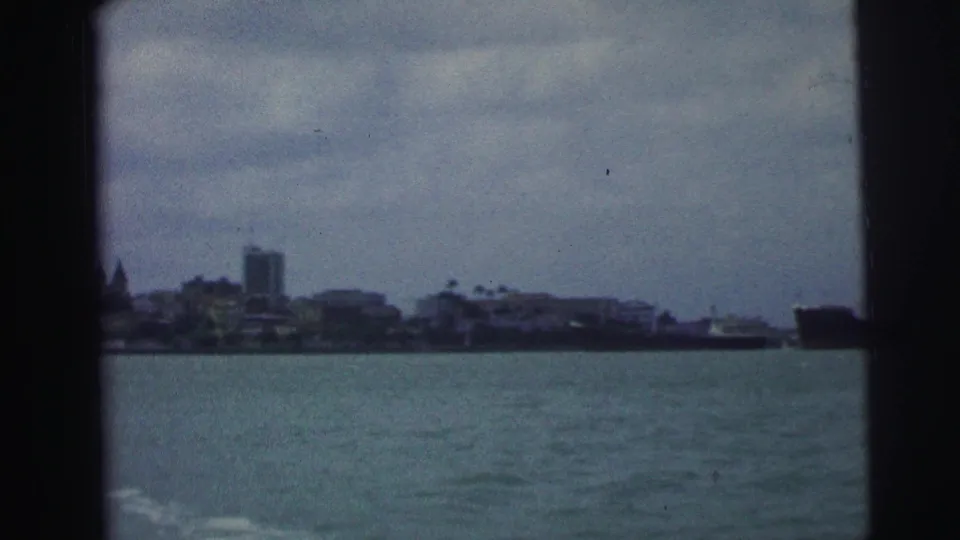 1967 Brazil 8mm frame showing a distant waterfront skyline across open water under a cloudy sky.