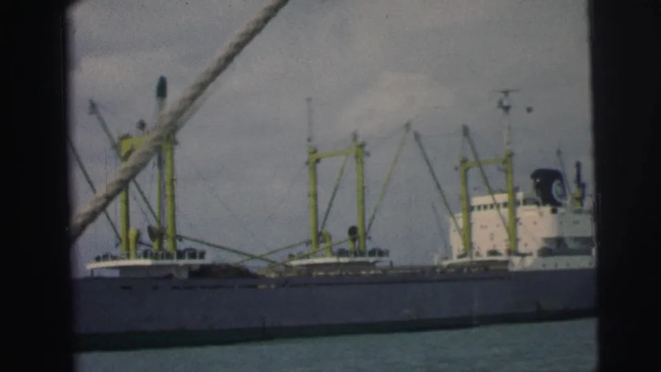 Large cargo ship at a Brazilian port in 1967, with yellow cranes and a white superstructure visible through 8mm film grain.
