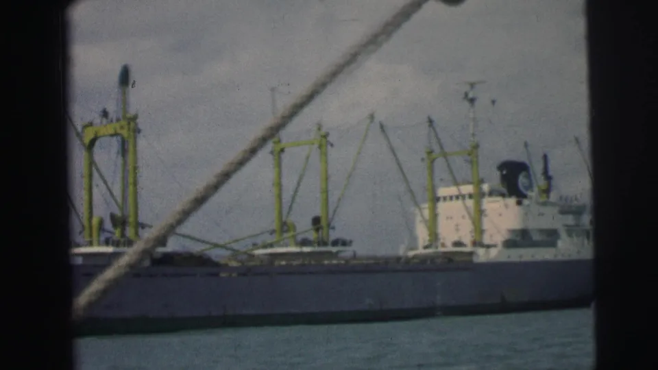 1967 Brazil 8mm frame showing a large cargo ship with yellow deck cranes and a white superstructure, filmed from a nearby boat.