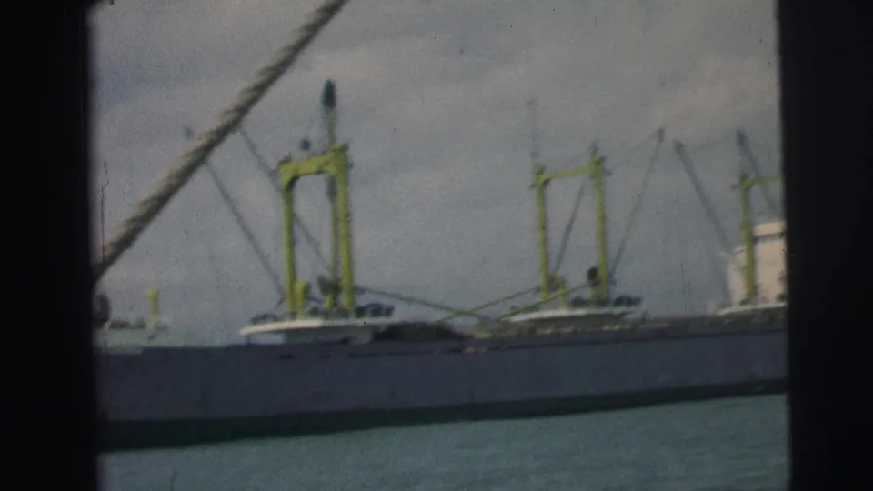 1967 Brazil home-movie view of a cargo ship’s side, with yellow cranes visible and boat rigging cutting across the frame.