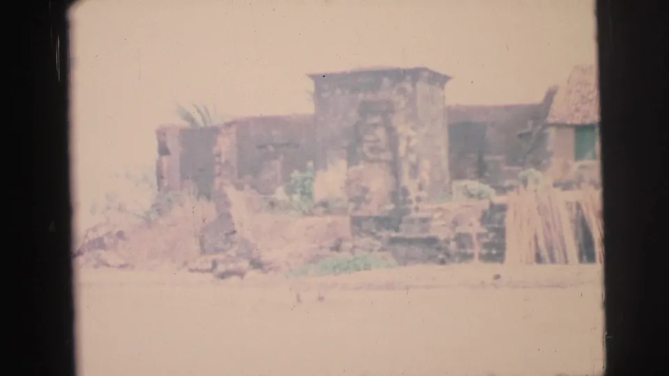 1967 Brazil home-movie frame of a rough stone coastal structure with stacked boards and bright shoreline exposure.
