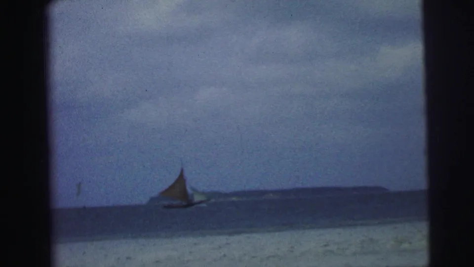 1967 Brazil 8mm home-movie view of a small sailboat against open blue water and a dark distant shoreline.