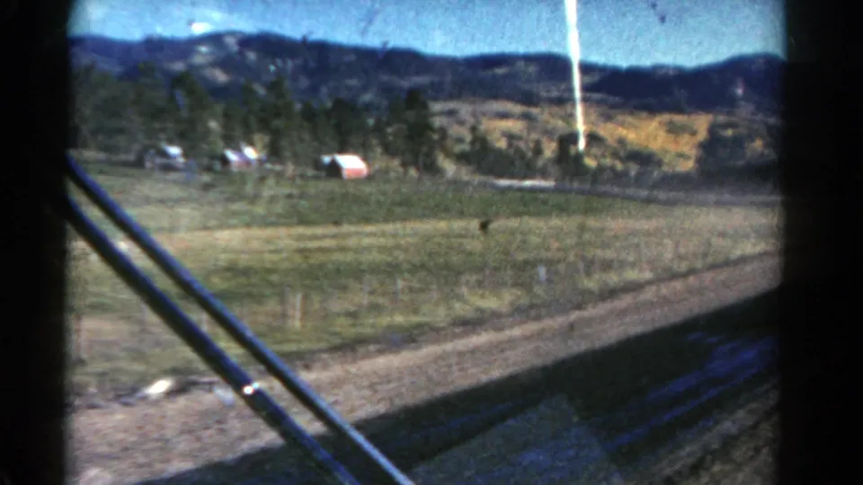 Motion-blurred 8mm view from a car in rural Colorado, showing fields, trees, low hills, and dark windshield wipers across the foreground.