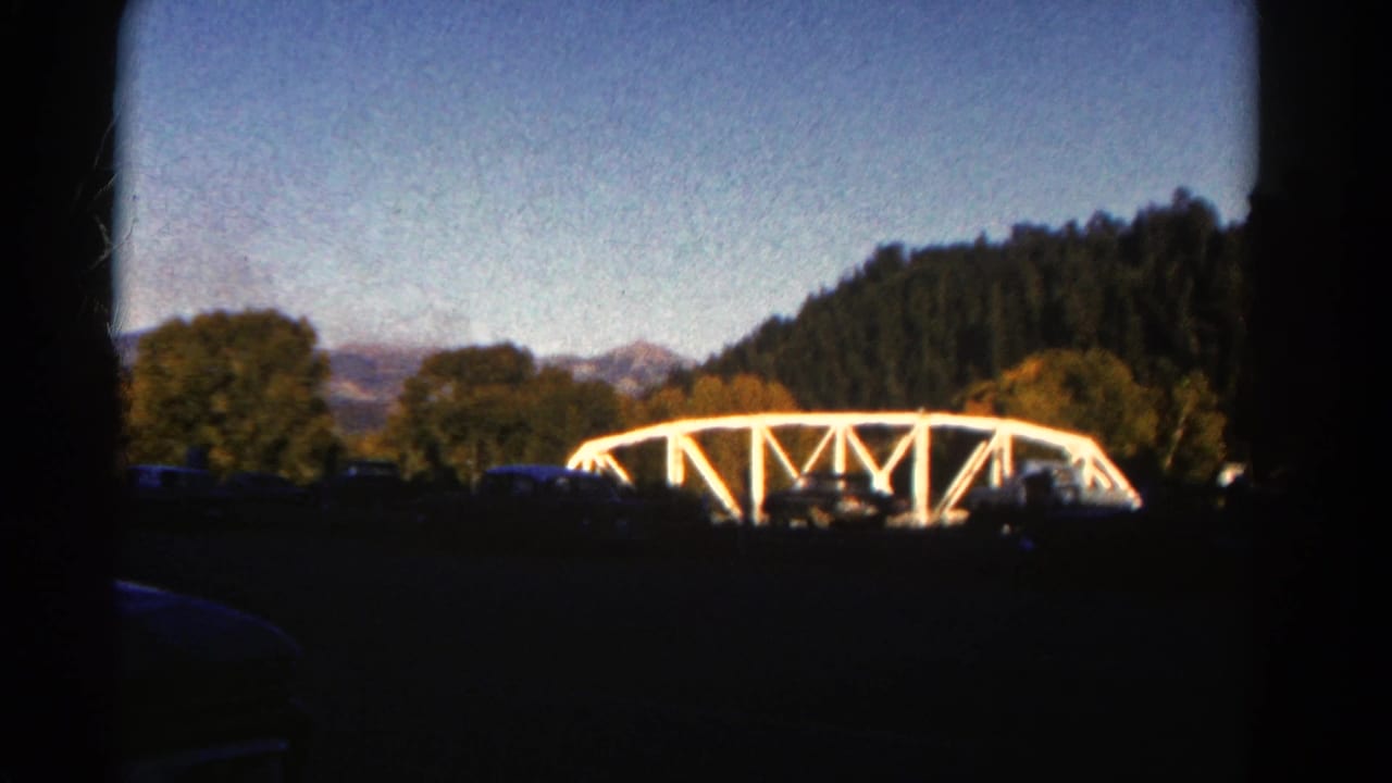 White bridge centered in a wooded landscape with mountains in the background.
