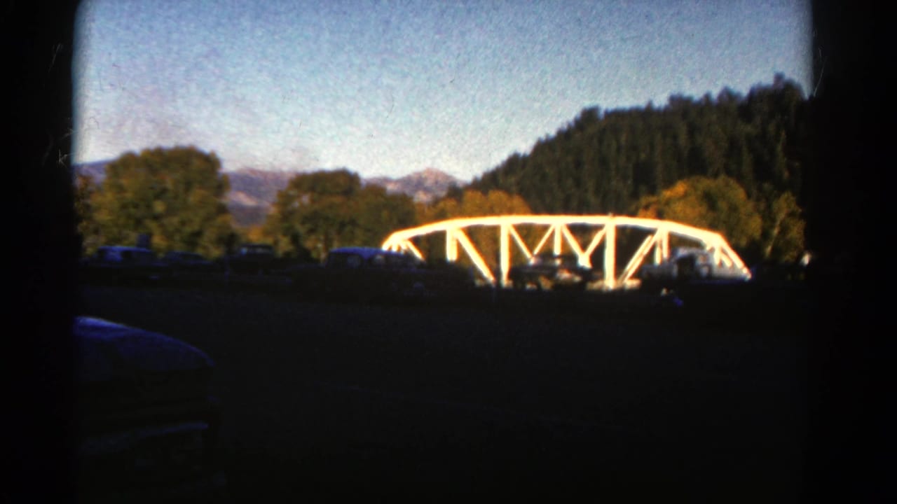 1967 Colorado 8mm frame showing a white truss bridge framed by trees, blue sky, dark vignette, and distant hills.