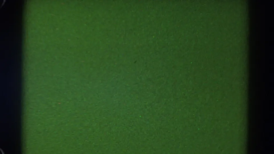 1967 Colorado 8mm frame showing a flat green field with dark film edges, fine grain, and scattered dust specks.