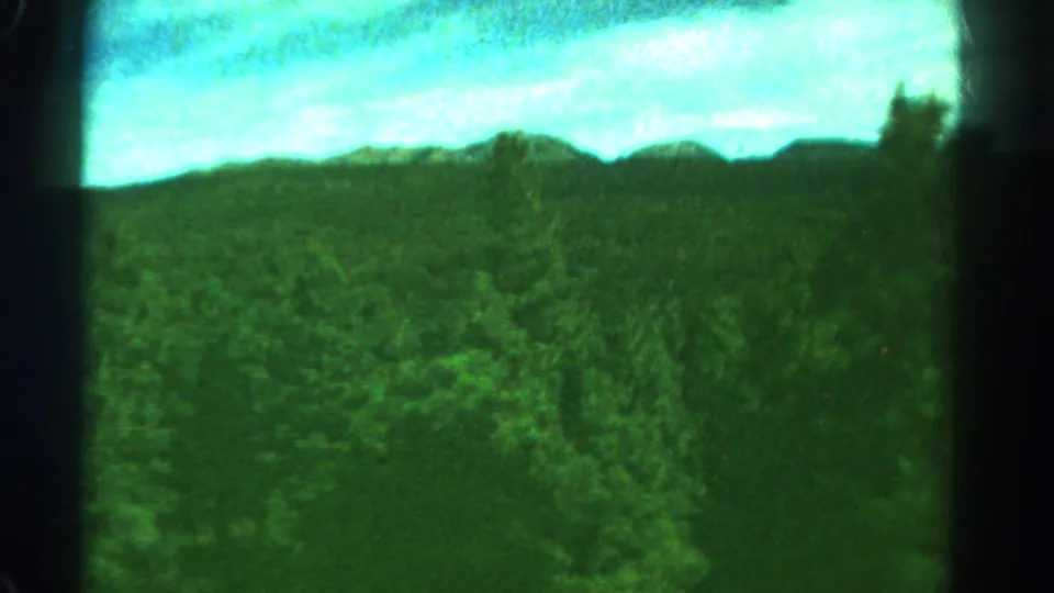 1967 Colorado home-movie view from a moving train, showing forested hills and bright sky through dark window framing.