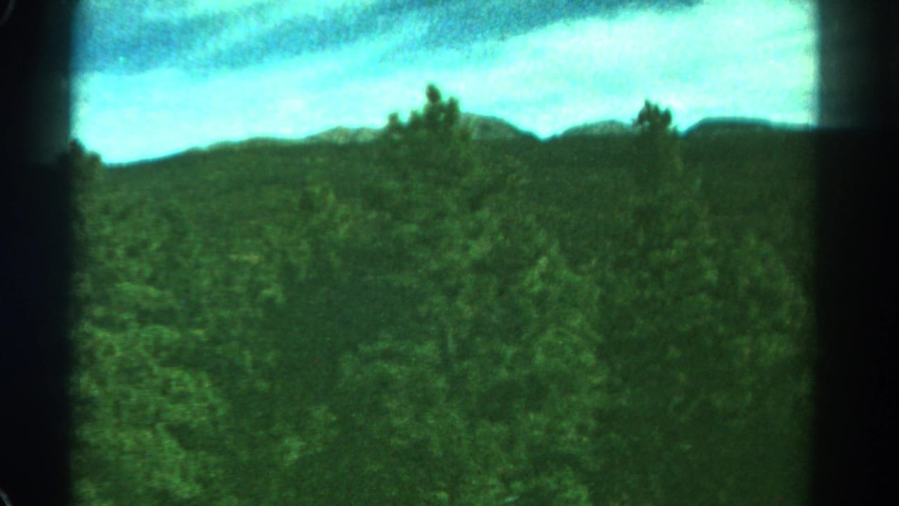 Green forested hillside beneath a bright cloudy sky with dark 8mm frame edges.