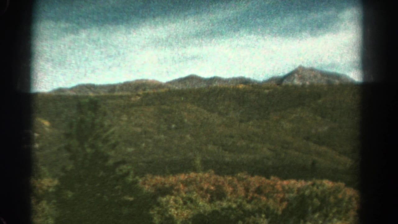 Colorado mountain landscape in faded 8mm color, with forested hills and ridgelines seen from a moving train.