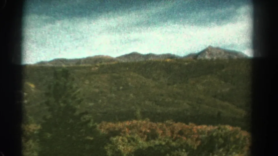 Colorado mountain landscape in faded 8mm color, with forested hills and ridgelines seen from a moving train.