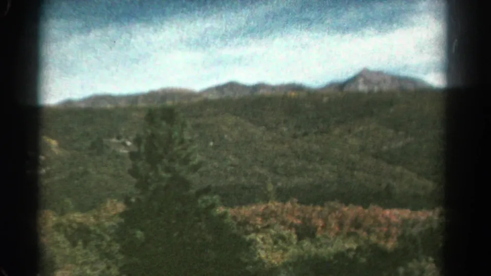 1967 Colorado 8mm still of an evergreen-lined valley and distant mountains, softly blurred by train motion.