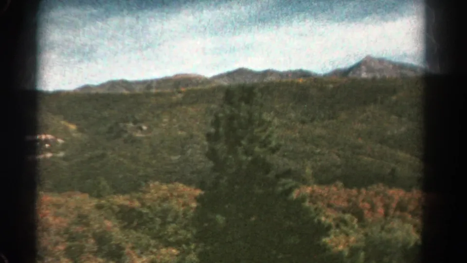 Faded 8mm view of Colorado hills and distant mountains from a moving train, with foreground trees crossing the frame.
