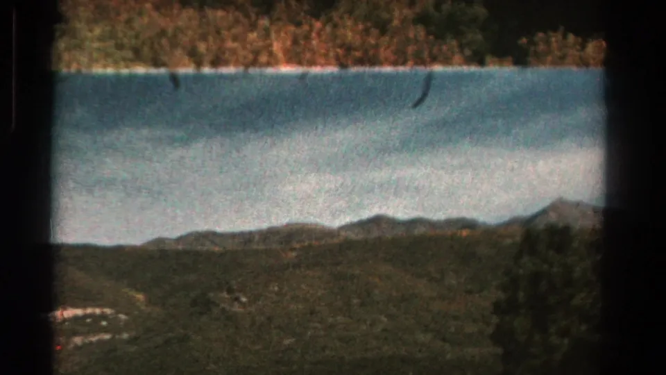 1967 Colorado 8mm frame with distant ridges, wooded slopes, blue water, and visible gate edges from the film scan.