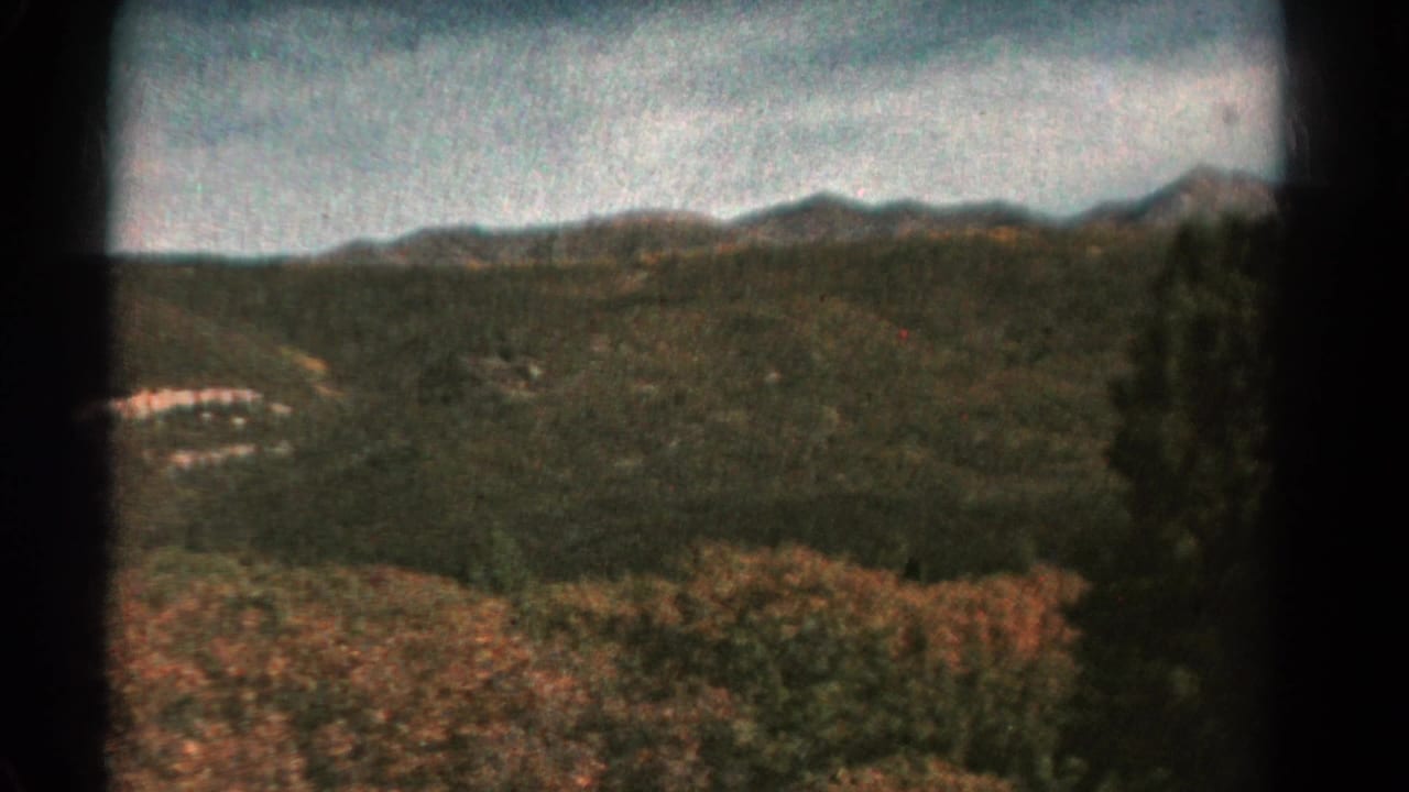 1967 Colorado home-movie view of forested hills, distant ridges, cloudy sky, and autumn-toned brush in the foreground.
