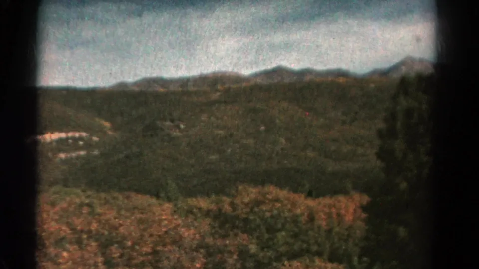 1967 Colorado home-movie view of forested hills, distant ridges, cloudy sky, and autumn-toned brush in the foreground.