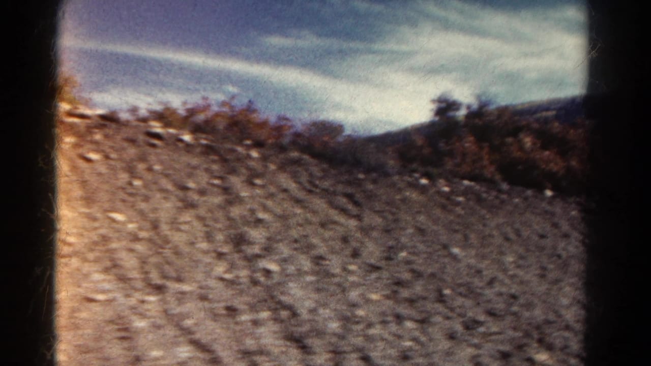 Rocky dirt roadside seen through a dark car window frame under blue sky.